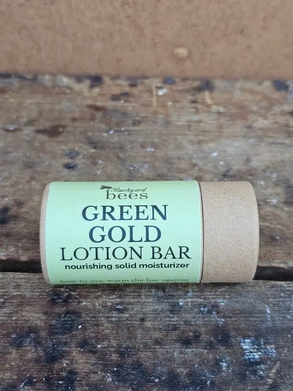 Green Gold beeswax lotion bar by Backyard Bees on a natural wood background with herbs.